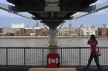 Comp image : lond010109 : Girl in jeans walking under the Millennium Bridge in London, England, with the opposite side of the River Thames in sunshine in the backgound