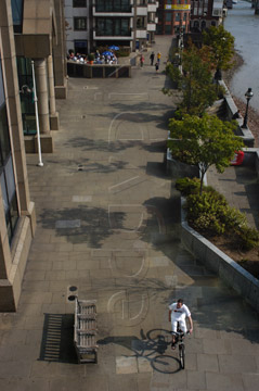 Comp image : lond010119 : Aerial view of a single cyclist in white on the paved walkway beside the River Thames in London, England, with sun casting shadows on the paving