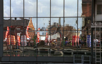 Comp image : mar000130 : London Marathon 2000: reflection of the runners and red sponsor's signs in the glass wall of a building in the Docklands area of London, at about half distance