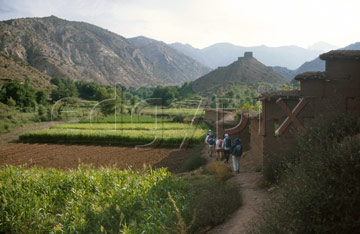 Comp image : mgun0423 : A small group of trekkers passes buildings in a Berber village in the fertile Ait Bougemez valley in the High Atlas mountains of Morocco; a grain store on a high mound in the mid distance