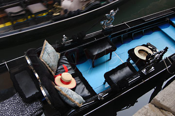 Comp image : ven021331 : Looking down on a gondola on a canal in Venice, Italy; a straw gondolier's hat with a red ribbon lies on the seat, and part of another gondola is seen passing in the background