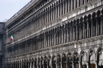 Comp image : ven021356 : The grey stone columns of the Procuratie Vecchie (built 1480 - 1517) in the Piazza San Marco [St Marks Square] in Venice, Italy, with an Italian flag flying in the distance