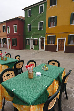 Comp image : ven021693 : A colourful table outside a cafe on the island of Burano, Venice, Italy, matches the brightly painted buildings on the other side of the street