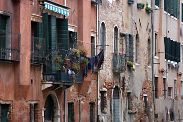 Comp image : ven021732 : Old red ochre buildings with jumbled windows beside a canal in Venice, Italy, with brick showing through the plasterwork, damaged by damp and high water