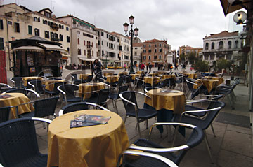 Comp image : ven021764 : Chairs and round tables with yellow tablecloths outside a cafe in Campo San Stefano in Venice, Italy; a traditional 3-light Venetian street light behind