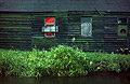 Dark, derelict old riverside building with a red painted boarded up window and green grass on the river bank Dark, derelict old riverside building with a red painted boarded up window and green grass on the river bank
