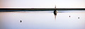 Panoramic image showing a fishing boat returning from sea on a flat calm waterway - a thin strip of land in the background - on the coast of Suffolk, England