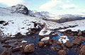 Snow-covered Crinkle Crags, Great Langdale, in the English Lake District, under a blue sky, with rocks in a stream in the foreground