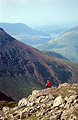 A walker in red rests in the summer sun on High Stile (over Buttermere) in the English Lake District. Red Pike in the background.