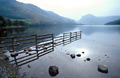 Morning autumn sun and reflection of a fence and rocks in the still surface of Buttermere lake, in the English Lake District, with Fleetwith Pike in the distance