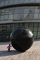 'Black ball' sculpture outside London's City Hall, dwarfing a tiny girl who is trying to move it