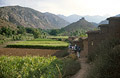 A small group of trekkers passes buildings in a Berber village in the fertile Ait Bougemez valley in the High Atlas mountains of Morocco; a grain store on a high mound in the mid distance