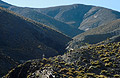 Looking up towards a peak in the High Atlas mountains of Morocco, with grass tufts in the foreground and a tiny lone figure standing in the mid distance