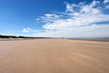 Flat deserted beach at low tide under a blue sky with scattered cloud, on the North Norfolk coast of England