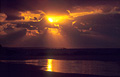 Dramatic orange sunset lighting up the clouds, and its reflection in the wet sea shore at low tide