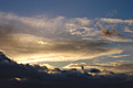 A heavy band of ominous dark cloud in a blue sky in front of the setting winter sun