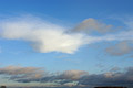 Wispy white cloud against an azure sky, with gathering gray clouds on the horizon