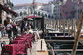Tables with red tablecloths at a cafe/restaurant by the Grande Canal [Canal Grande] in Venice, Italy, with the Rialto Bridge in the distance