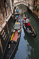 Gondolas passing in a narrow canal in Venice, Italy, with a bridge in the background; one moored, the other with a gondolier