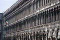 The grey stone columns of the Procuratie Vecchie (built 1480 - 1517) in the Piazza San Marco [St Marks Square] in Venice, Italy, with an Italian flag flying in the distance